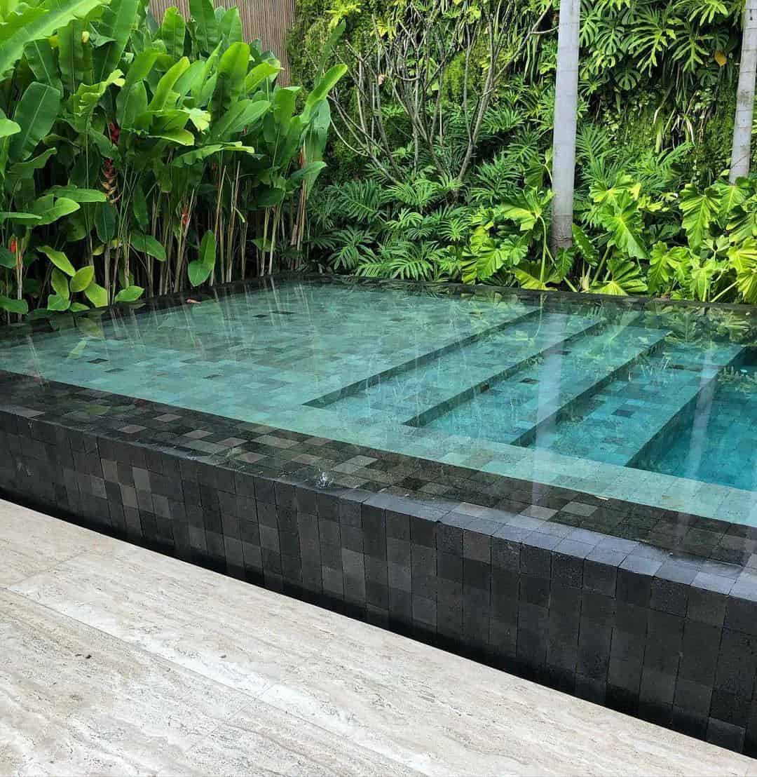 Piscina revestida em Pedra Hijau com borda em Pedra Hitam e jardim tropical